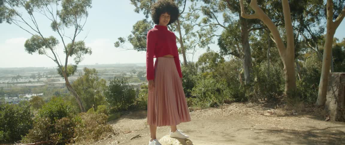 Young woman wearing a long skirt balancing over a rock in a trail on the mountain