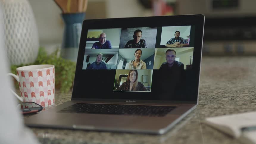 A person at home video chats with eight people on a laptop