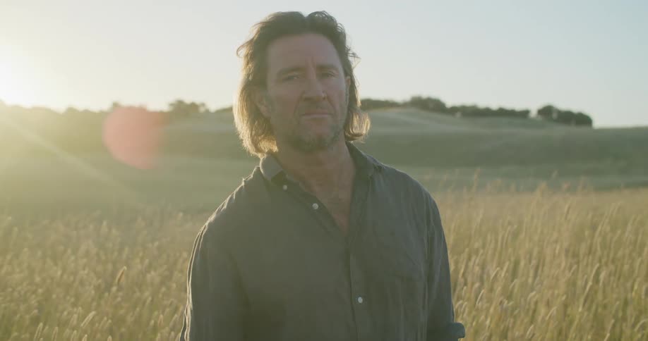 A man is standing in a grassland area at dusk