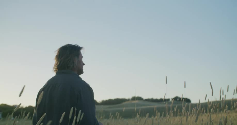 A man is walking outdoors in a grassland area at dusk