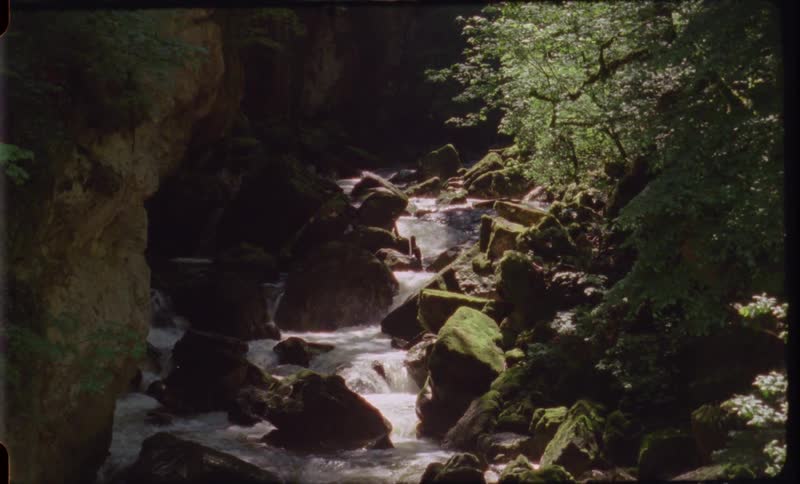 The current of a river flows around large stones in the wilderness during the day