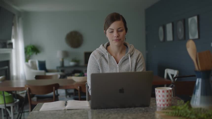 A young woman at home looks at her computer and takes notes