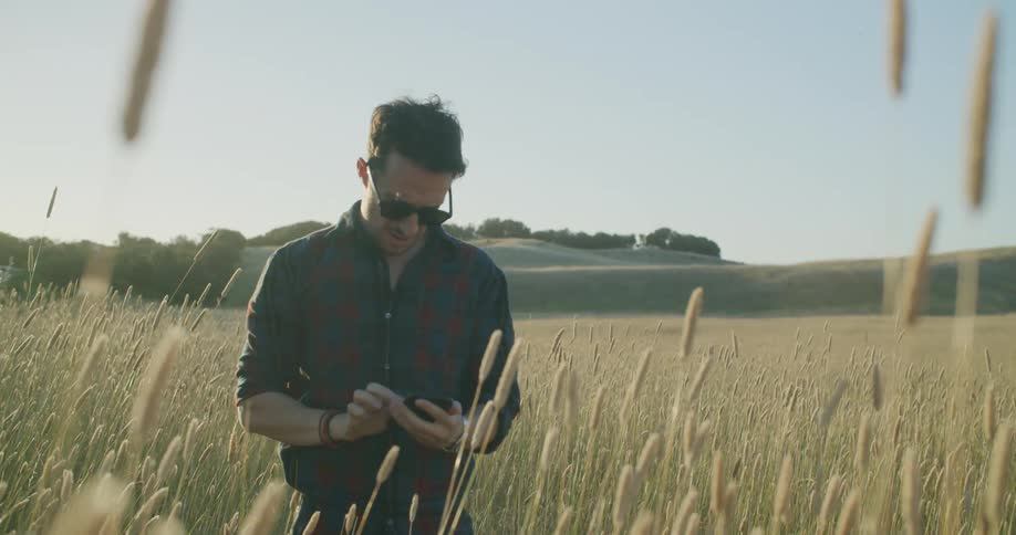 A man is looking at a cell phone while standing in a rural area