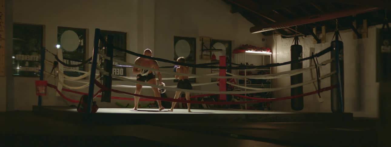 A strong muscular man teaching a young kid how to box in a gym