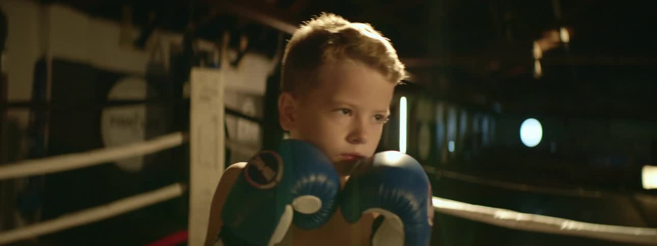A young boxer trains with an older man in a gym