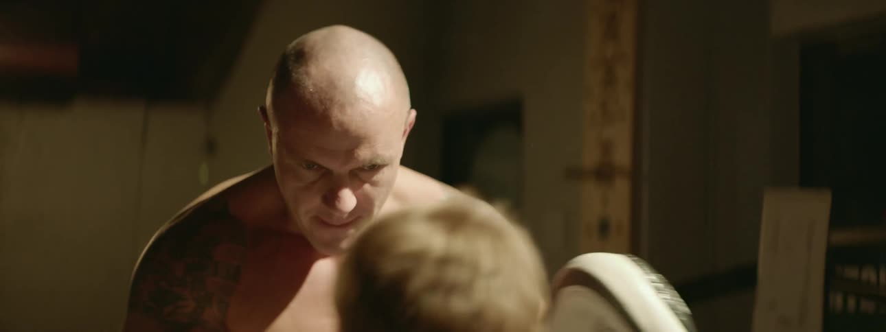 Strong shirtless muscular man teaching a boy how to box inside a ring on a gym