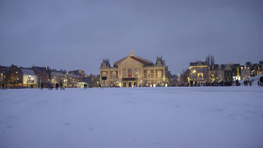A town with people with the ground covered with snow with buildings the sky and clouds in the background