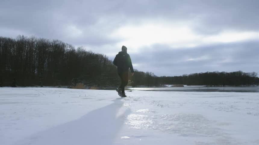 A man walking over the ice on a lake near the forest at sunset
