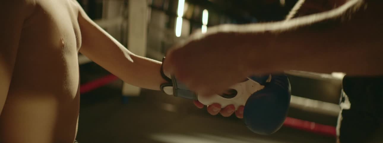 Male adult putting sparring gloves on a child inside boxing ring