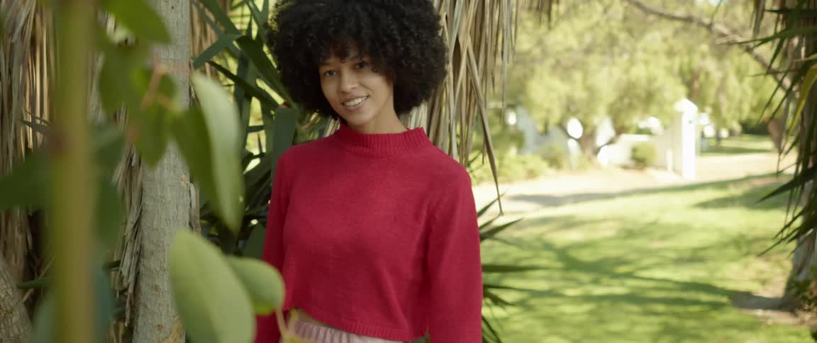Young woman wearing a red sweater models for the camera in a park