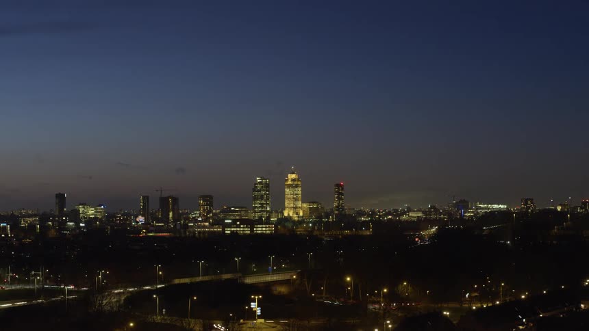 Traffic moves along a freeway through a metropolis as the sky grows darker