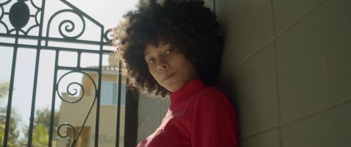 Young woman with an afro reclined on a wall looking at the camera