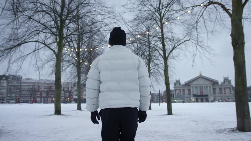 Man wearing a white parka walks among the decorated trees in a park at winter