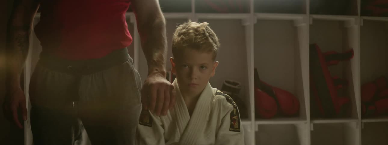 A boy and a man in a locker room with shelves and boxing gloves in the background