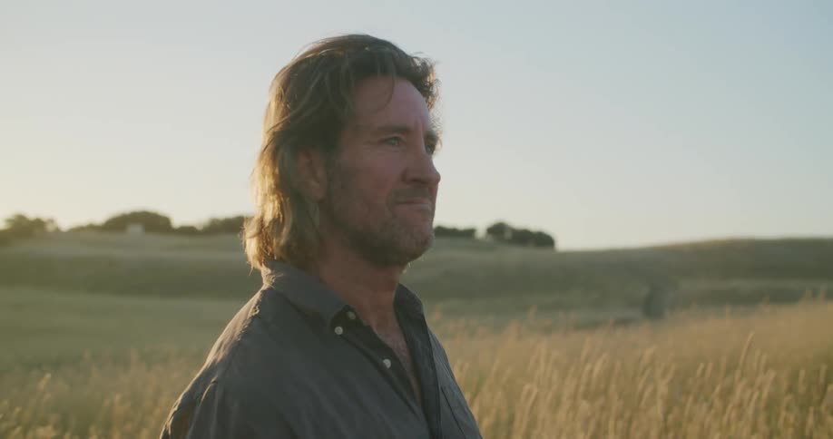 A man smiling while standing in a grassy field on a sunny day