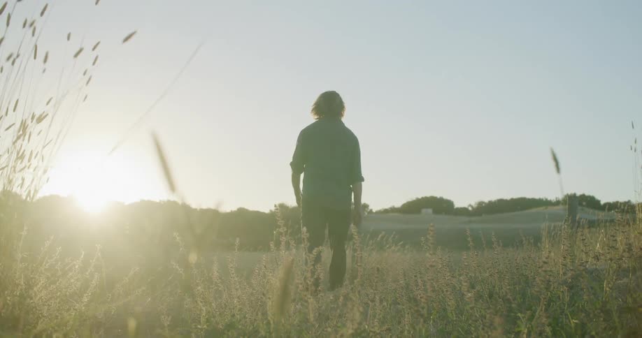 Man walks away toward hills and a building in a grassy field