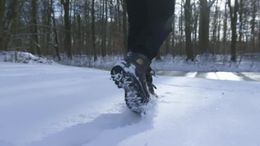 A person walking over the snow near a frozen river on the forest at sunset
