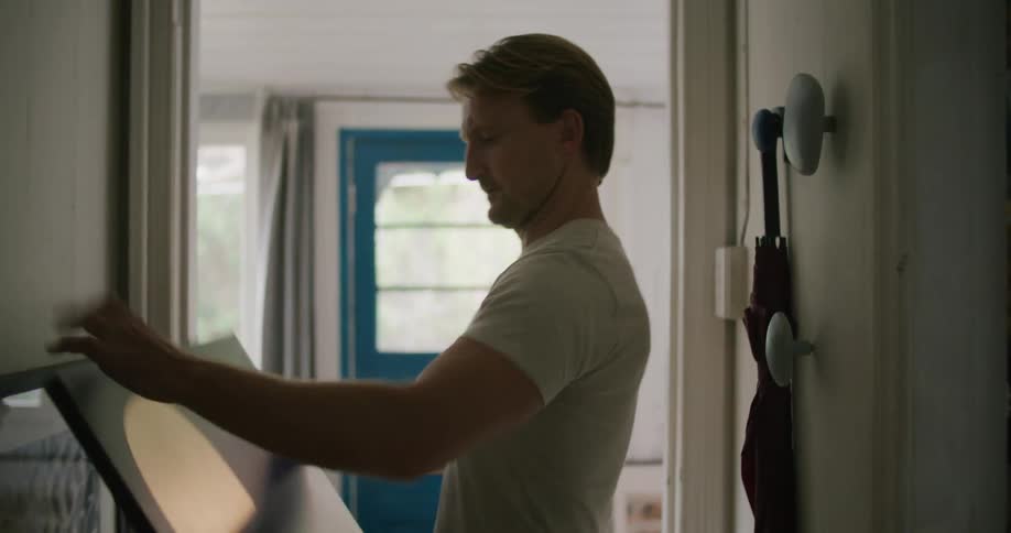 A man is walking through a house and putting a picture on the wall