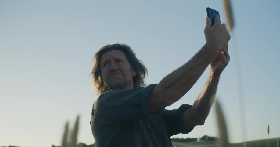 A man standing in a field holds up his cell phone as he searches for a signal