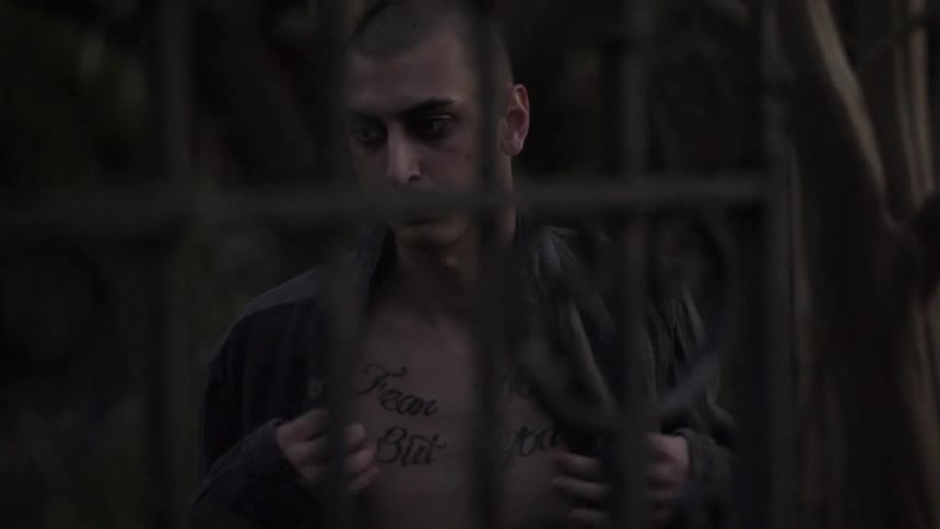 A tattooed man takes off his shirt