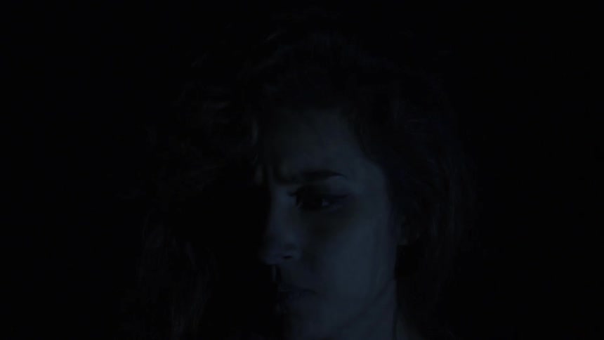 Woman stands in darkness while light flickers across her face