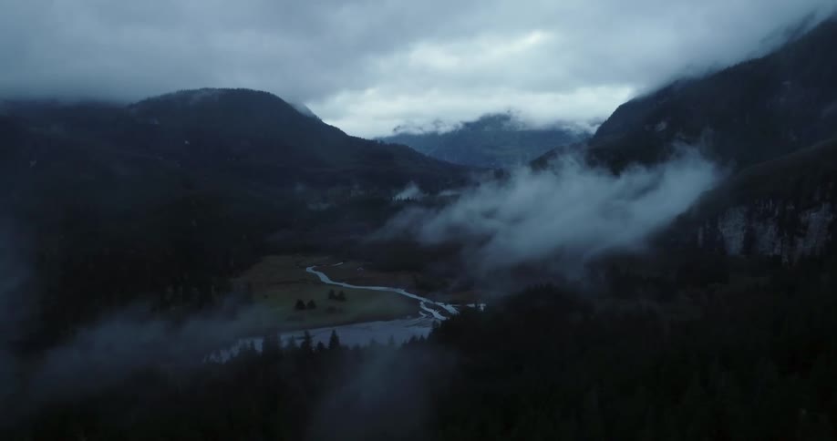 Dense fog and heavy clouds hang over a mountain range in a rural area