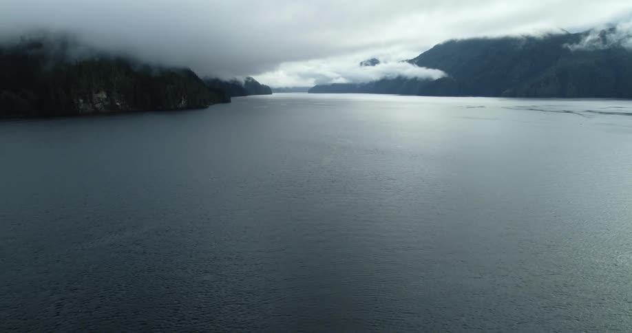 Aerial view of a lake near the cloud covered peaks of a mountain range