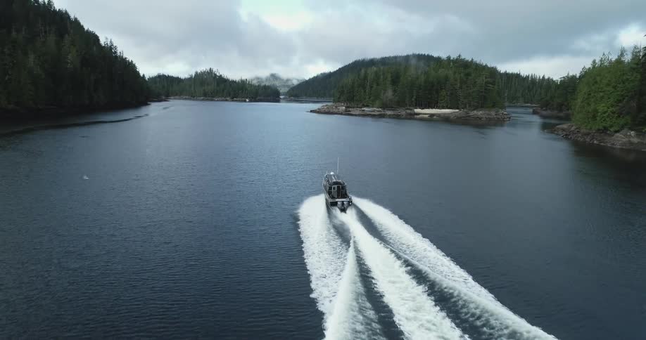 Boat cutting through river bordered by forest covered mountains leaves large wake