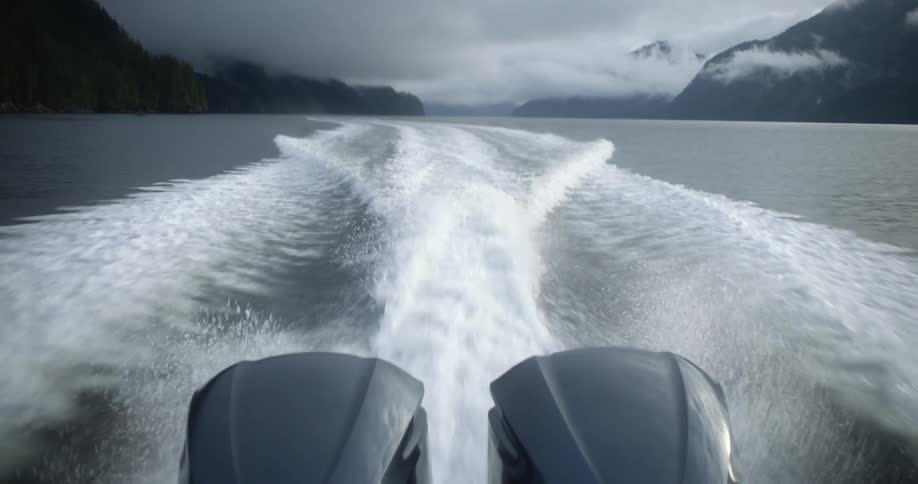 A boat with twin motors on a lake with land the sky and clouds in the background
