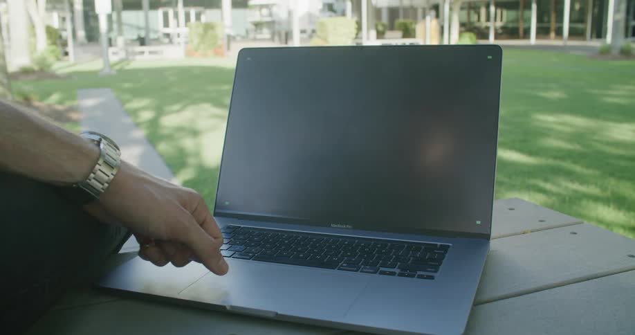 A person sitting over a table in the park in front of a laptop with a replaceable screen