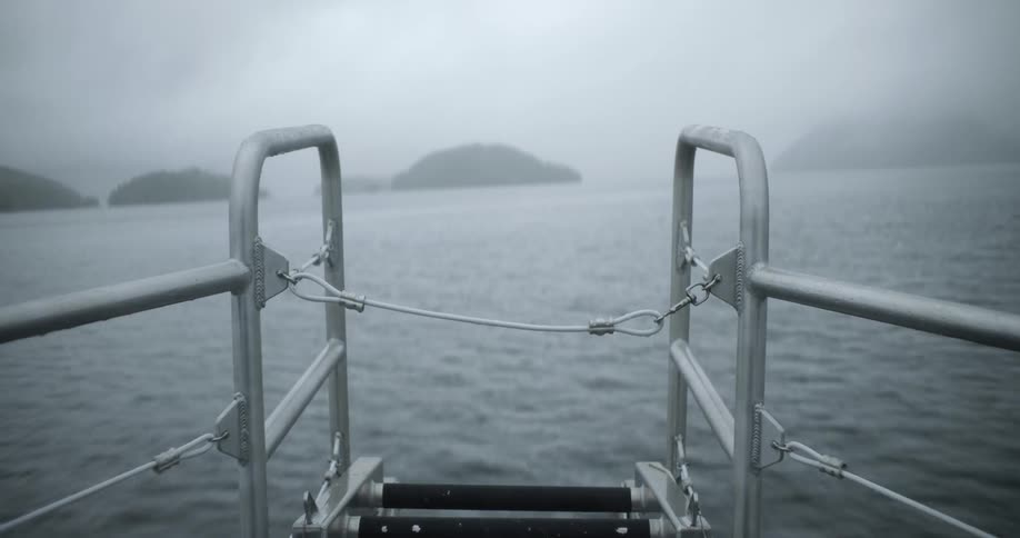 Railing in the bow of a boat sailing among the mist covered island on a lake