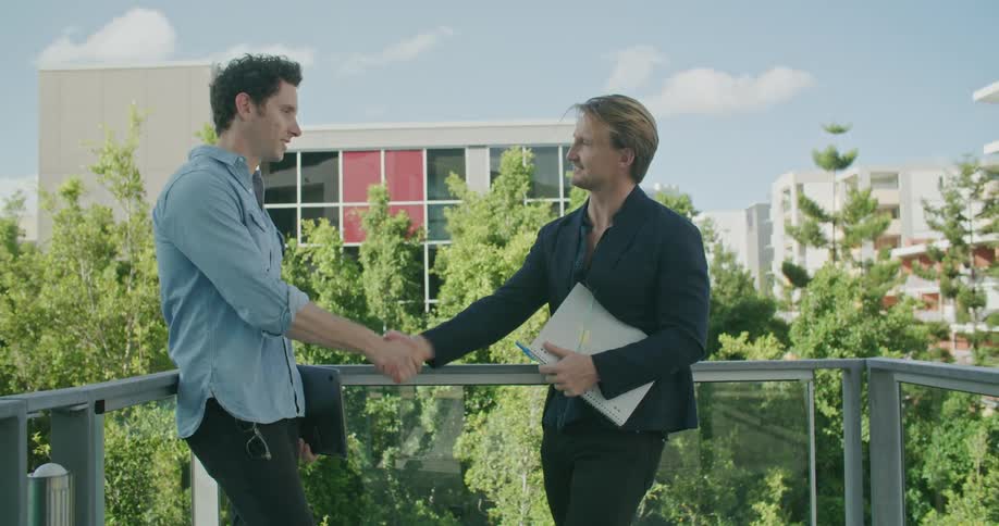 Men meeting on balcony overlooking other buildings shake hands