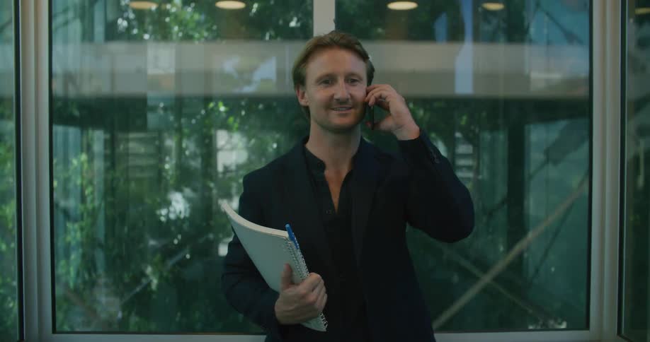 A man riding a glass panoramic elevator talking on the phone