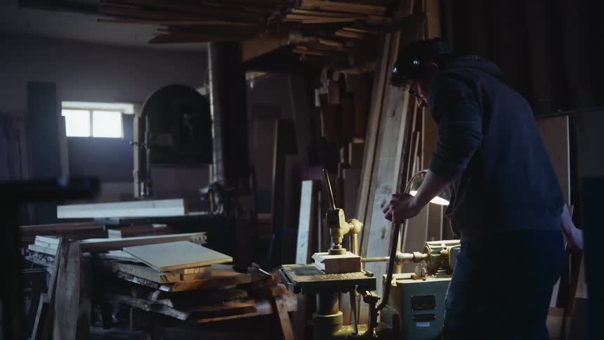 Man turns drills wood in dim workshop