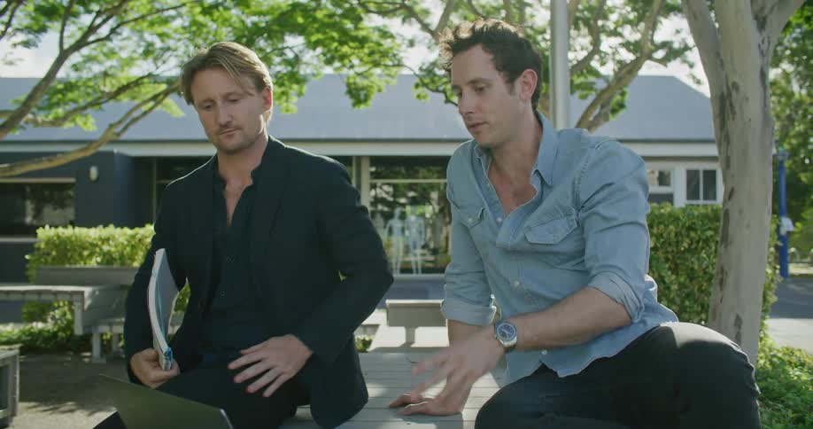Men sit on table outside talking about what is on a laptop
