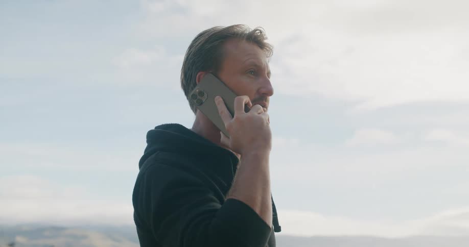 A man pacing while talking on a phone and drinking coffee outside