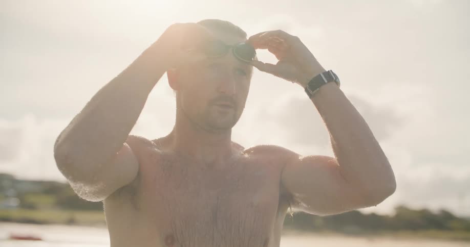 Man standing in lake putting on swim goggles