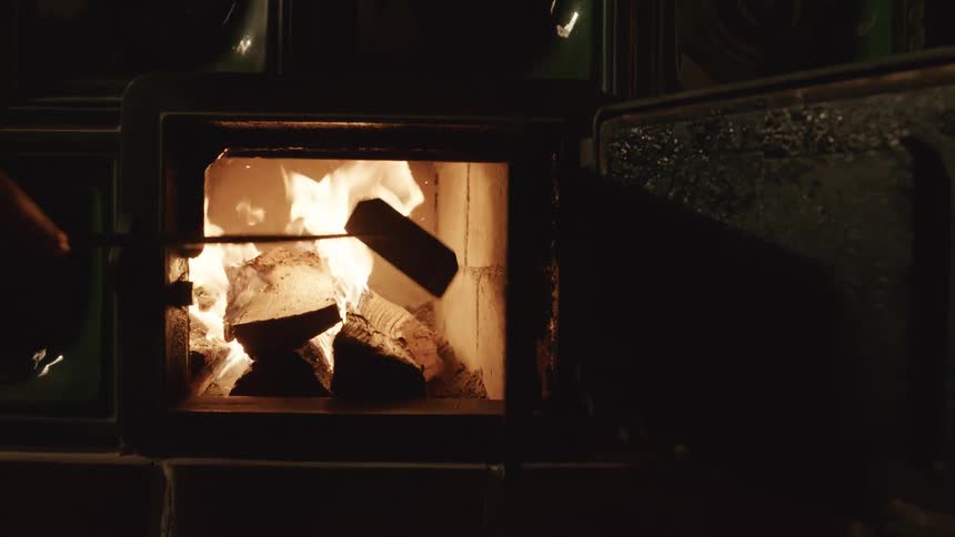 A person is putting logs in the wood stove