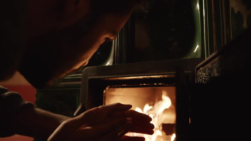 A man warming his hands by a wood burning fireplace