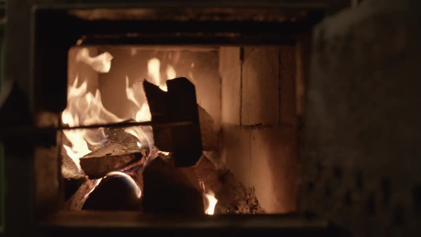 Pieces of burning wood are moved with a long rake in a furnace