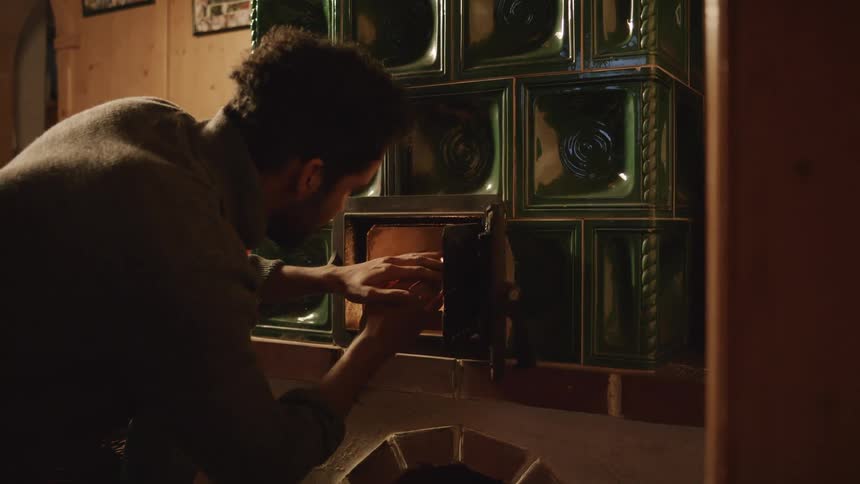 A young man warms his hands on the fire on a small oven over the fireplace