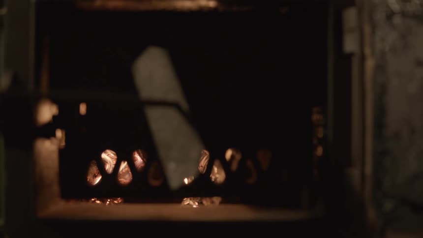A shovel moves the burning flaming wood inside a furnace and the door is closed