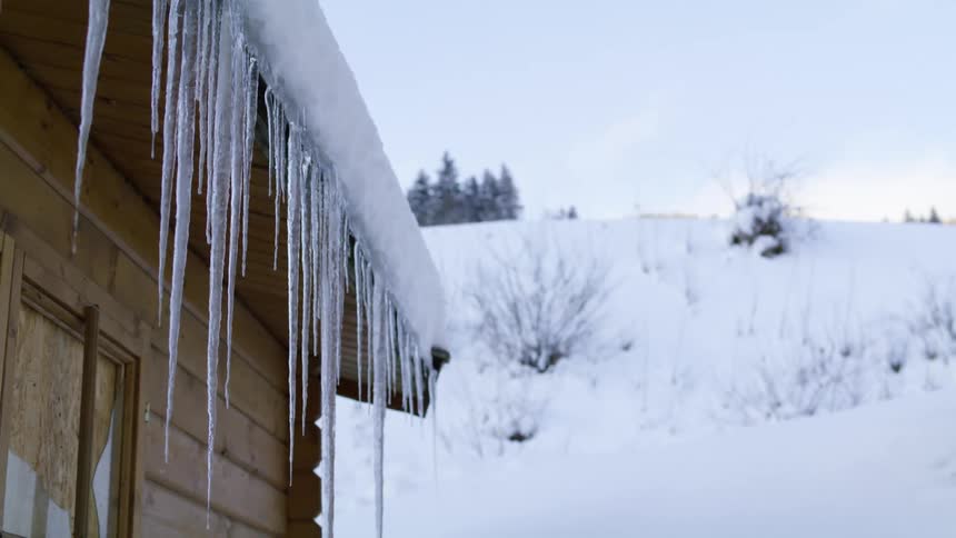 Icicles hanging from the edge of the roof of a cabin at winter