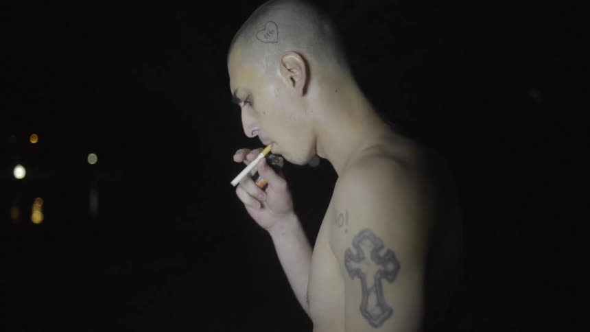 A shirtless man smokes a cigarette