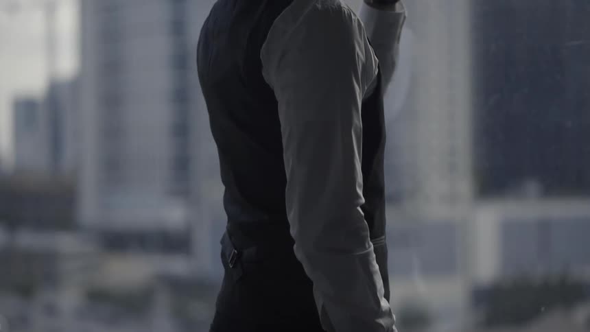 A man having a drink near a large window in an urban area