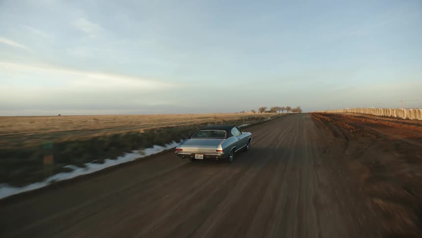 A car drives a long a road next to a wide open field