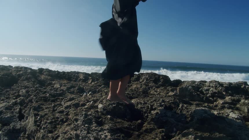 A woman is standing on the rocks of the beach