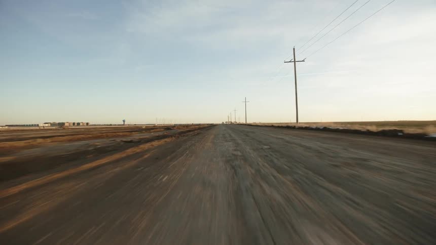 A road next to a grassy field and utility poles with the sky and clouds in the background