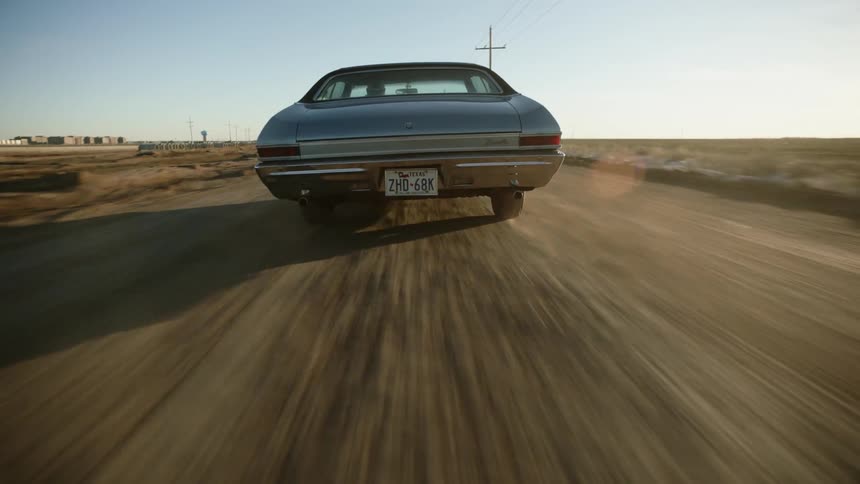 A blue vintage automobile speeds down a dirt road