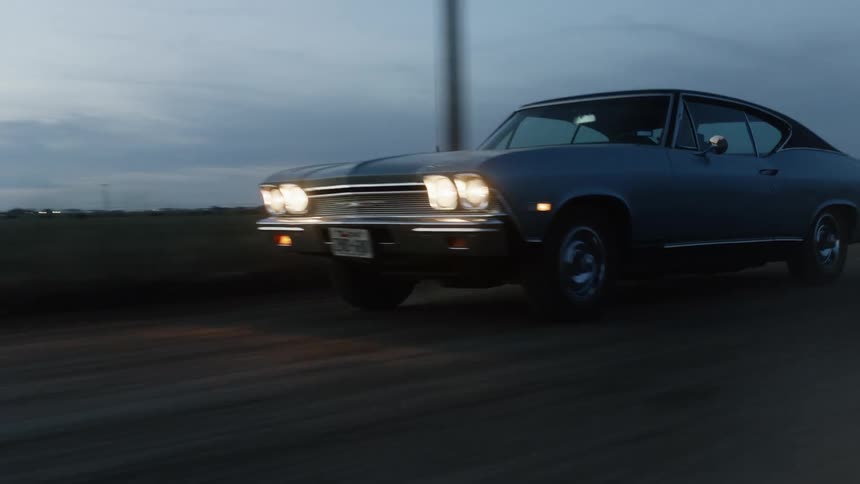 A car is driving in a rural area at dusk